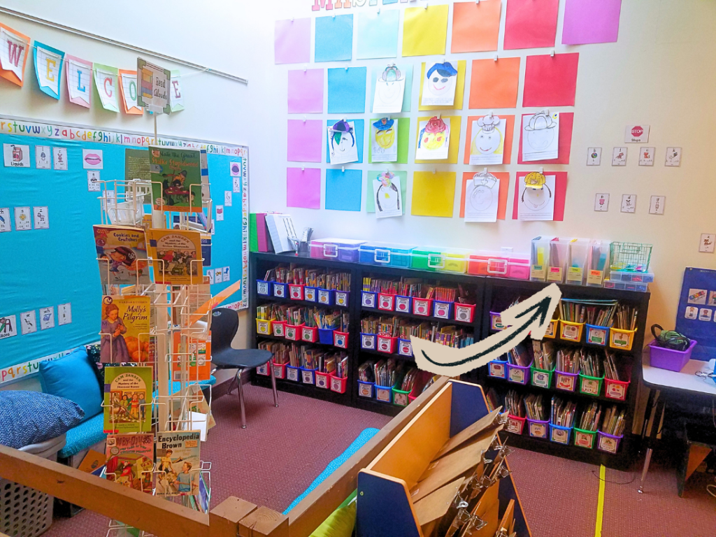 A colorful classroom with a 'Welcome' banner, featuring a bookshelf filled with books, a display of student artwork on the wall, and a cozy reading area with cushions.